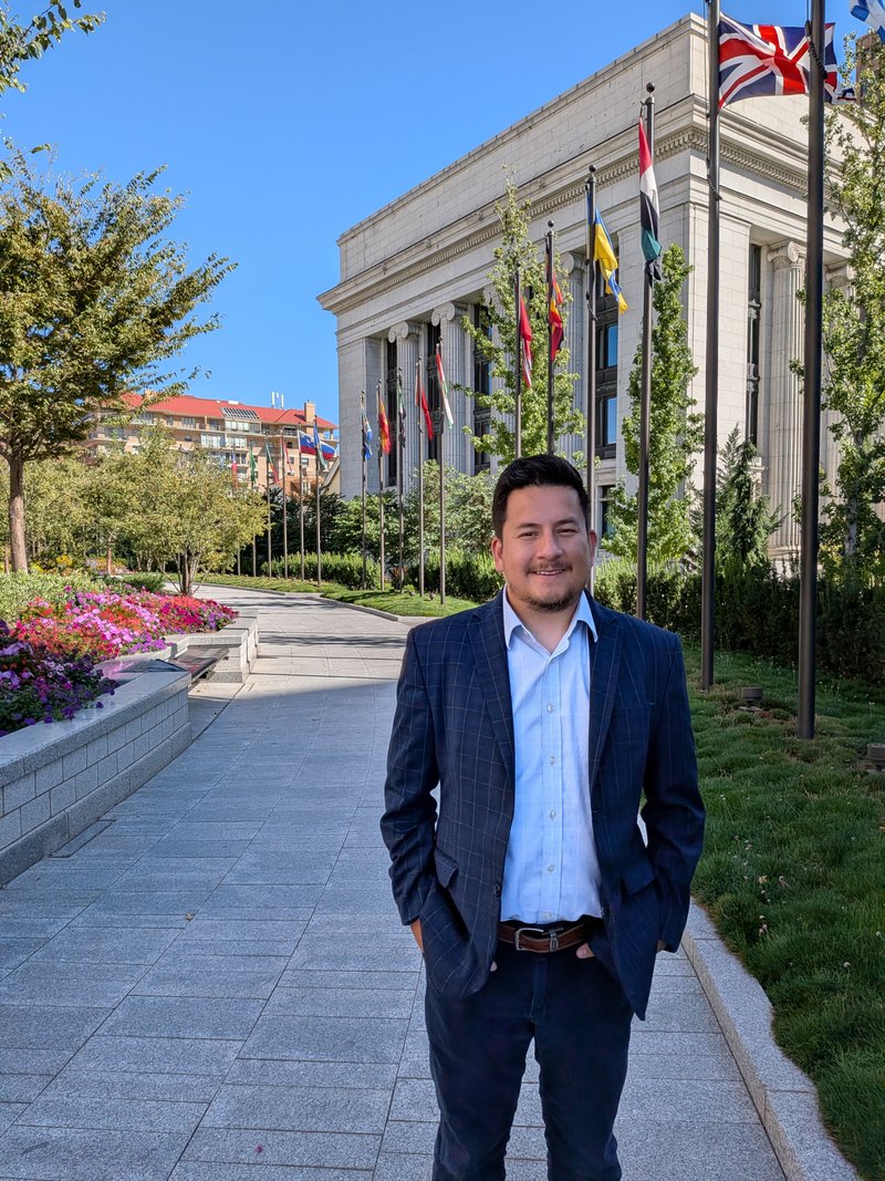 Mosiah Olvera on a walkway beside a row of international flags outside a stone government building