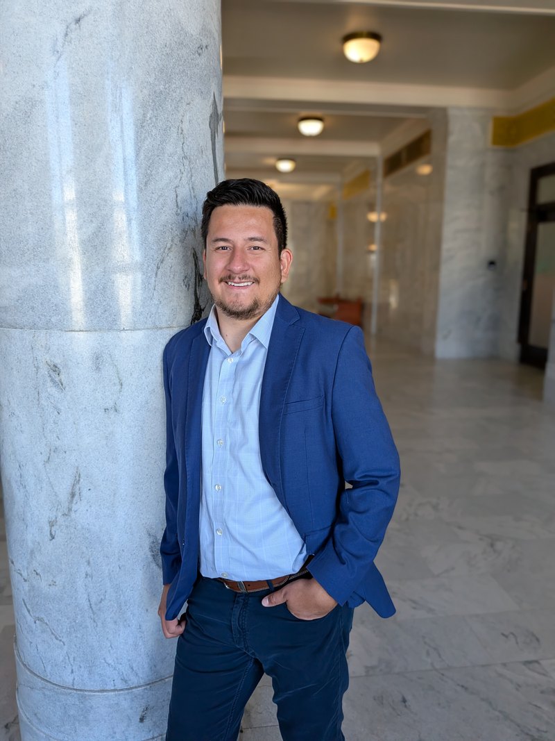 Mosiah Olvera in a blue suit jacket, leaning against a marble column in a public building corridor