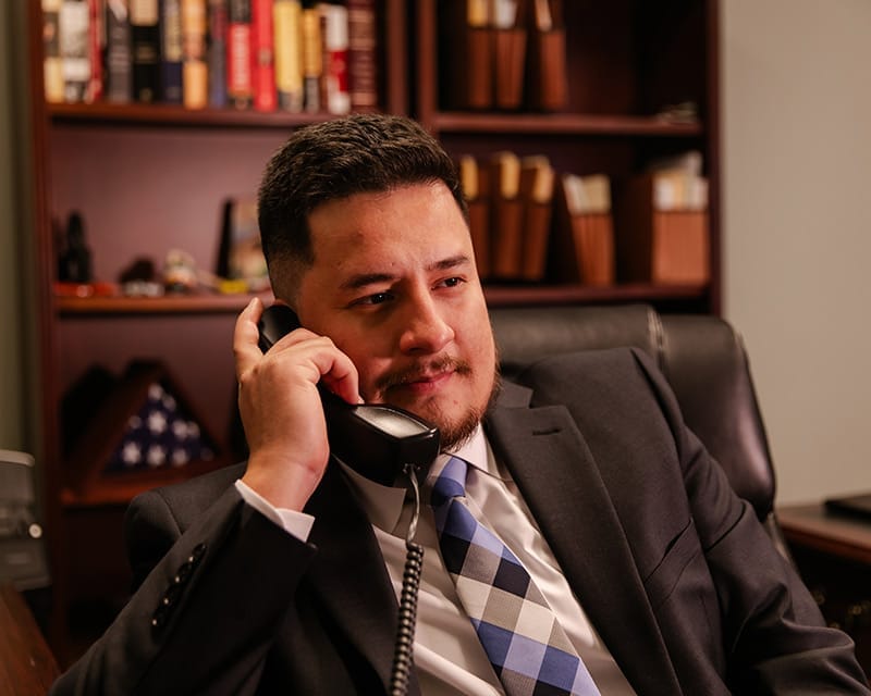Mosiah Olvera at his desk on the office phone, a wall of law books behind him