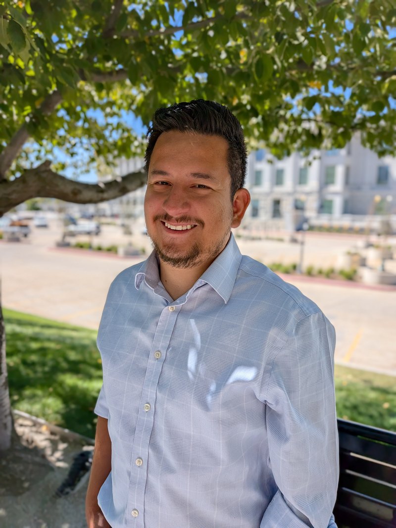 Mosiah Olvera smiling in the shade of a tree on a downtown sidewalk